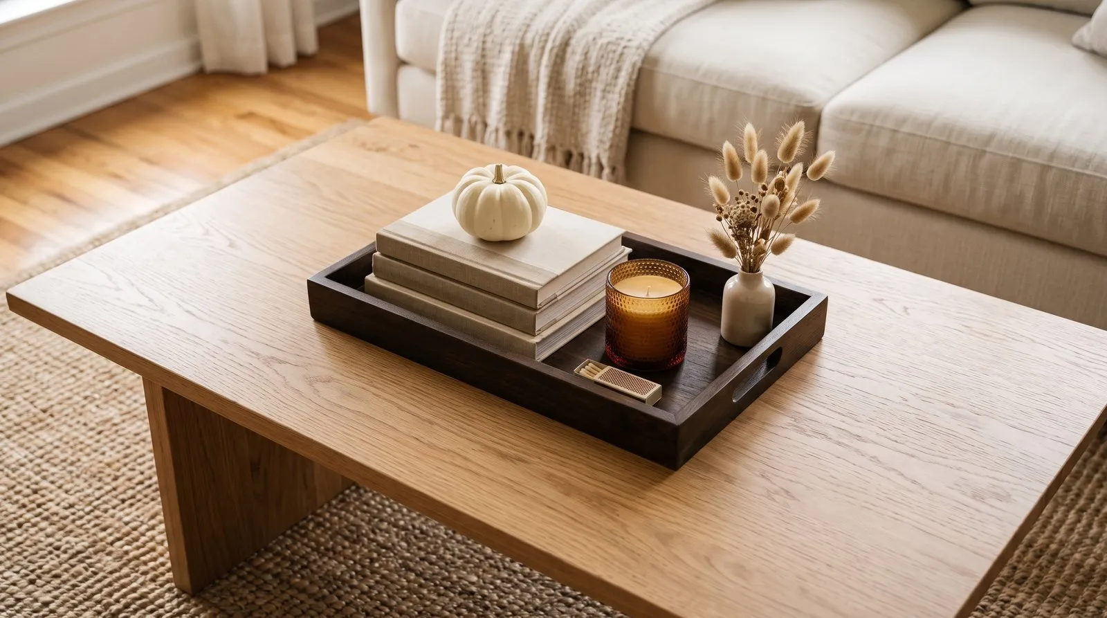 Wooden coffee table tray styled with a pillar candle, books, and a single mini white pumpkin.
